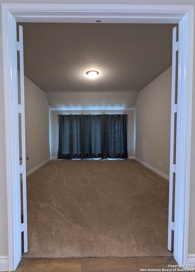 carpeted spare room with vaulted ceiling and a textured ceiling