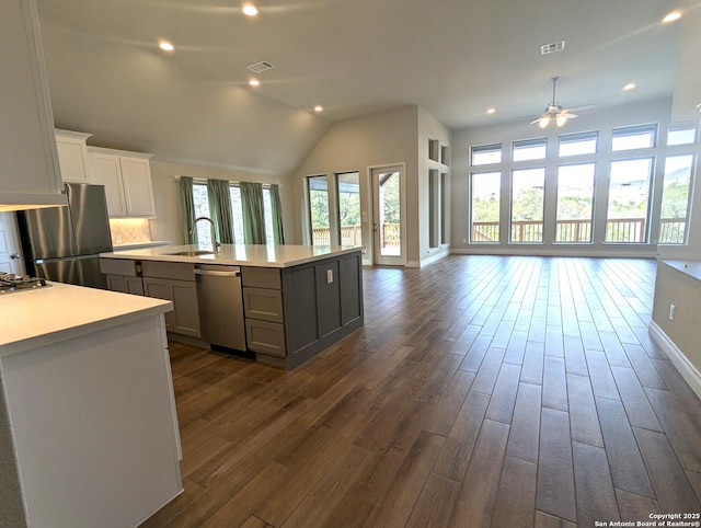 kitchen with gray cabinets, appliances with stainless steel finishes, an island with sink, backsplash, and dark wood-type flooring