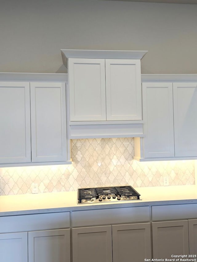 kitchen featuring backsplash, stainless steel gas stovetop, white cabinets, and premium range hood