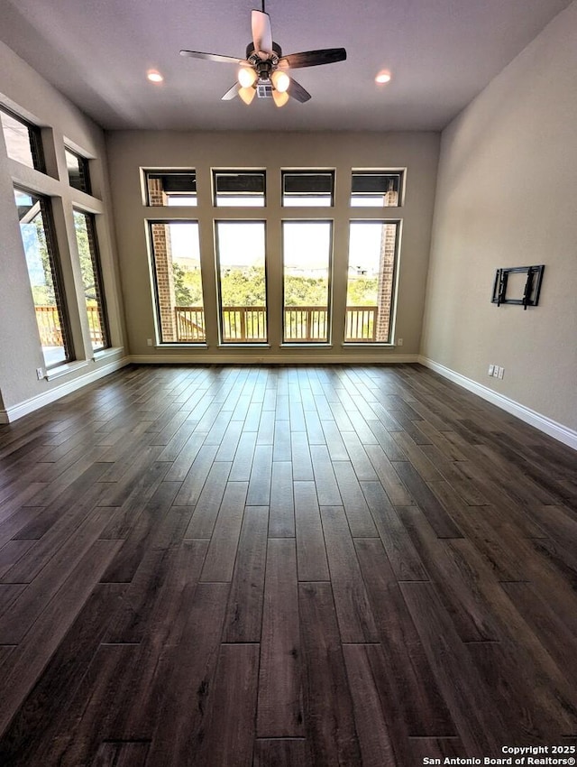 empty room with a wealth of natural light, dark wood-type flooring, and ceiling fan