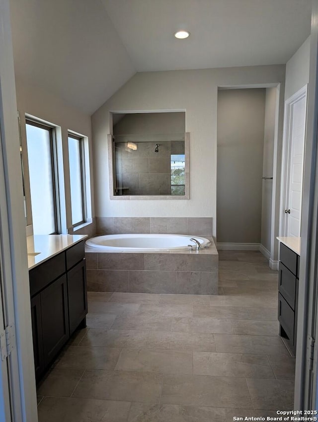 bathroom with vanity, lofted ceiling, and tiled bath