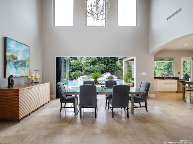 dining space with a towering ceiling, plenty of natural light, sink, and a notable chandelier