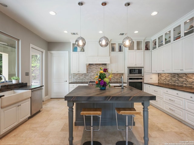 kitchen featuring pendant lighting, stainless steel appliances, a kitchen island with sink, and white cabinets