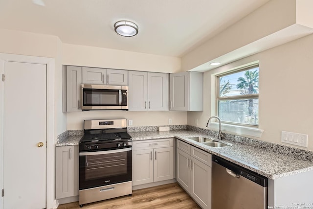 kitchen featuring stainless steel appliances, light stone countertops, sink, and light hardwood / wood-style floors