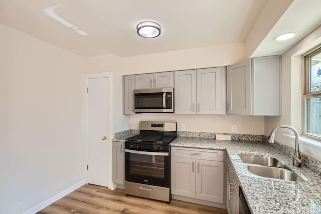 kitchen with sink, light hardwood / wood-style flooring, appliances with stainless steel finishes, gray cabinetry, and light stone countertops