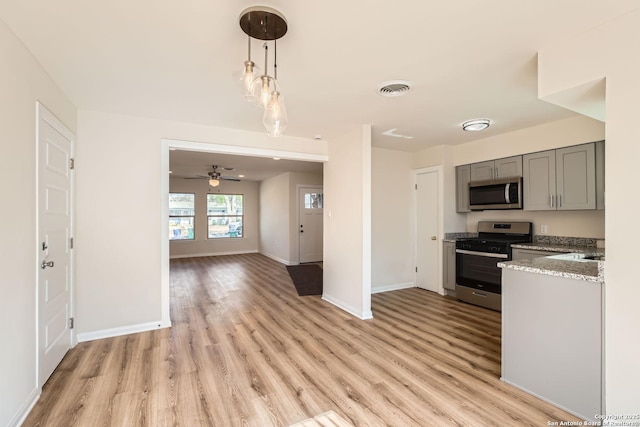 kitchen with gray cabinets, hanging light fixtures, stainless steel appliances, light stone counters, and light hardwood / wood-style floors