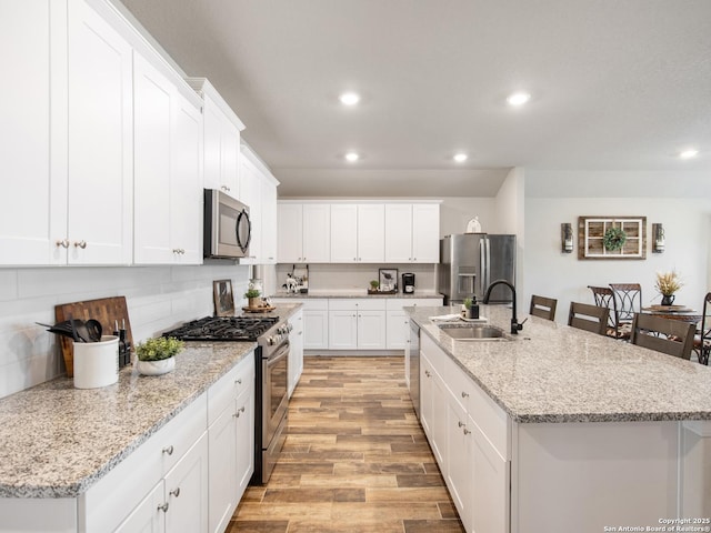 kitchen featuring sink, white cabinetry, light stone counters, appliances with stainless steel finishes, and a kitchen island with sink