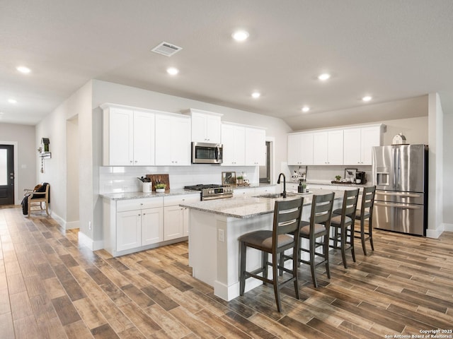 kitchen featuring white cabinetry, tasteful backsplash, stainless steel appliances, light stone countertops, and a kitchen island with sink