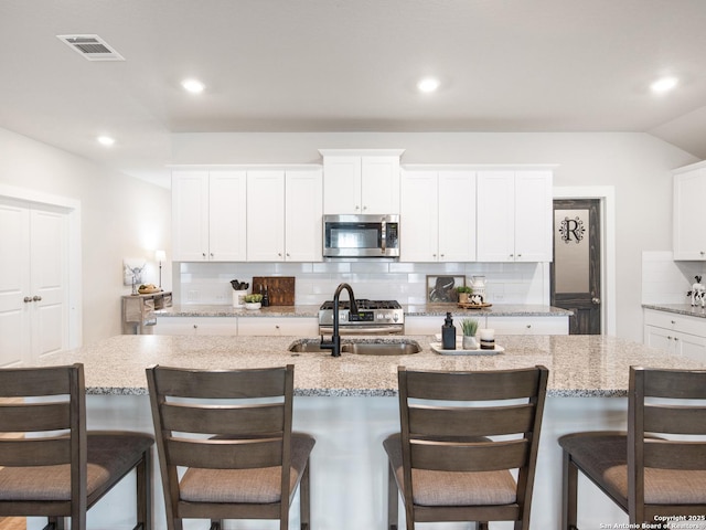 kitchen with sink, a breakfast bar area, a kitchen island with sink, white cabinetry, and stainless steel appliances