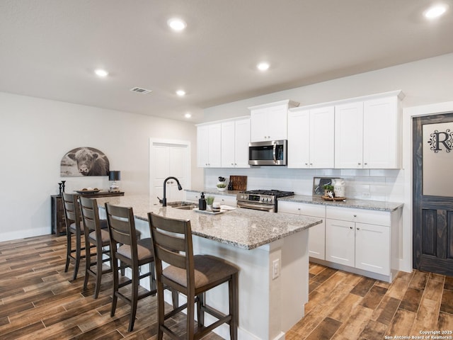 kitchen with a kitchen bar, sink, white cabinetry, stainless steel appliances, and a kitchen island with sink