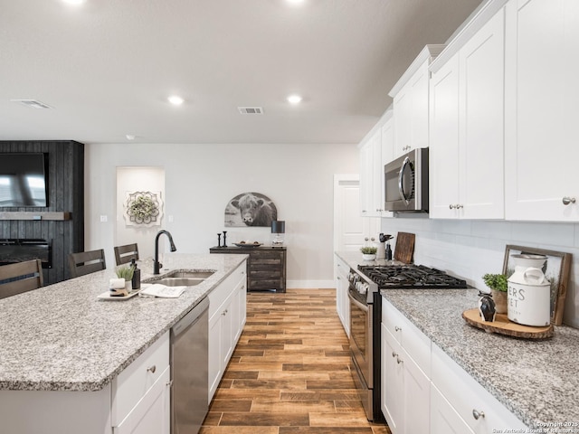 kitchen featuring sink, light wood-type flooring, an island with sink, stainless steel appliances, and white cabinets