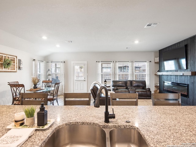 kitchen with vaulted ceiling, sink, a large fireplace, and light stone counters