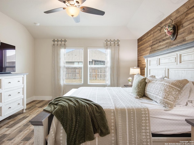 bedroom featuring ceiling fan, lofted ceiling, wooden walls, and hardwood / wood-style floors