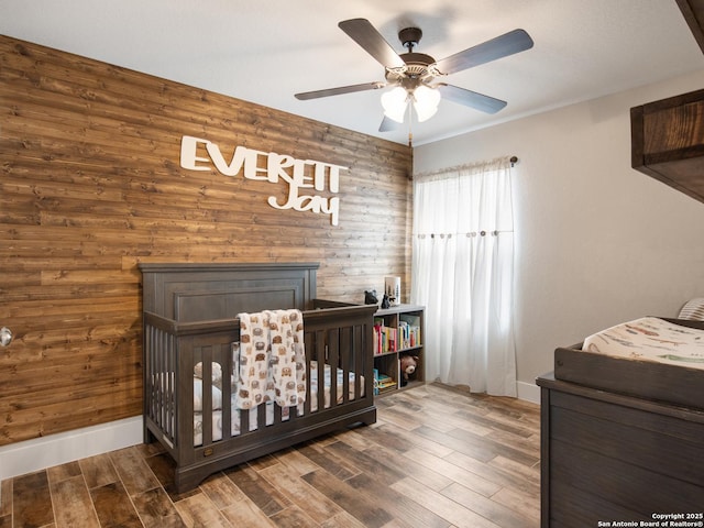 bedroom with a fireplace, dark wood-type flooring, a nursery area, and ceiling fan