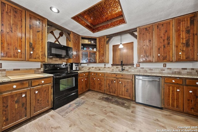 kitchen featuring pendant lighting, black appliances, sink, light hardwood / wood-style floors, and a tray ceiling