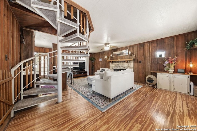 living room featuring hardwood / wood-style floors, a stone fireplace, ceiling fan, and wood walls