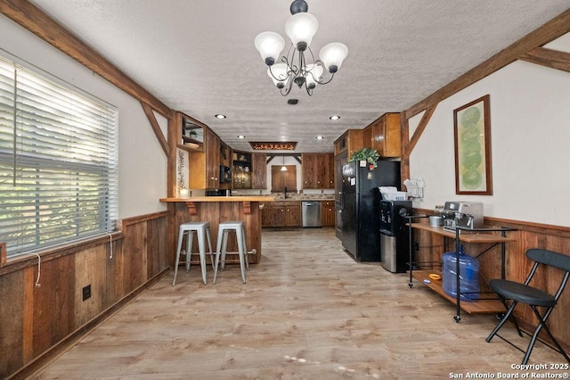 kitchen with a kitchen bar, light wood-type flooring, black refrigerator, stainless steel dishwasher, and kitchen peninsula