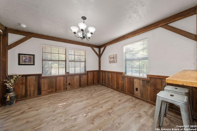 dining area featuring a chandelier, vaulted ceiling, a textured ceiling, and light hardwood / wood-style flooring