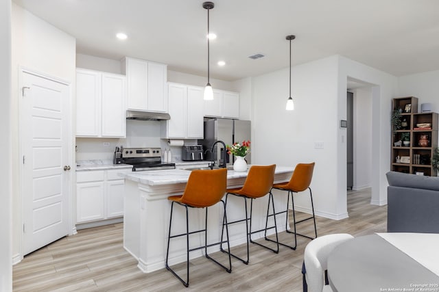 kitchen with appliances with stainless steel finishes, a kitchen island with sink, light wood-type flooring, and decorative light fixtures