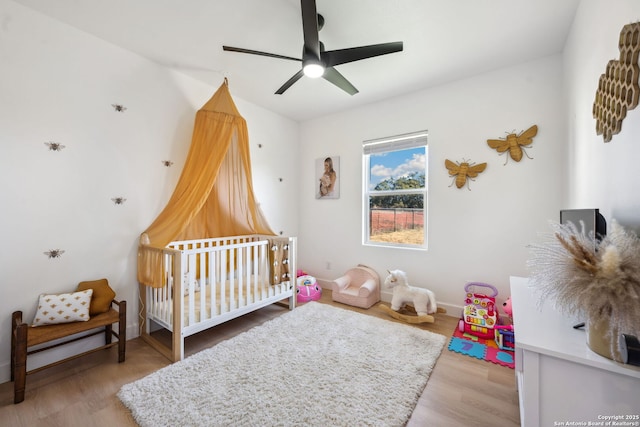 bedroom featuring light hardwood / wood-style flooring, a crib, and ceiling fan