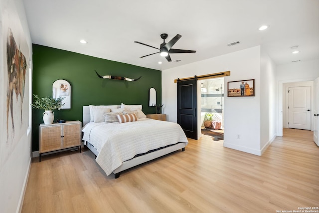 bedroom featuring ceiling fan, a barn door, and light wood-type flooring