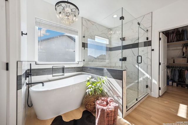 bathroom with tile walls, wood-type flooring, a chandelier, and separate shower and tub