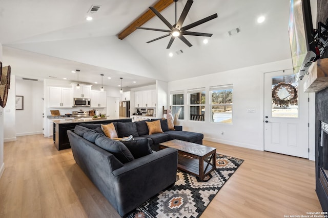 living room featuring a tile fireplace, high vaulted ceiling, beamed ceiling, ceiling fan, and light hardwood / wood-style floors