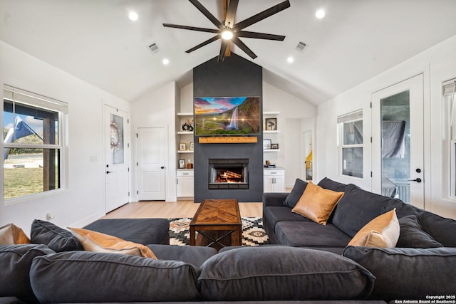 living room featuring lofted ceiling with beams, a fireplace, light hardwood / wood-style floors, and built in shelves