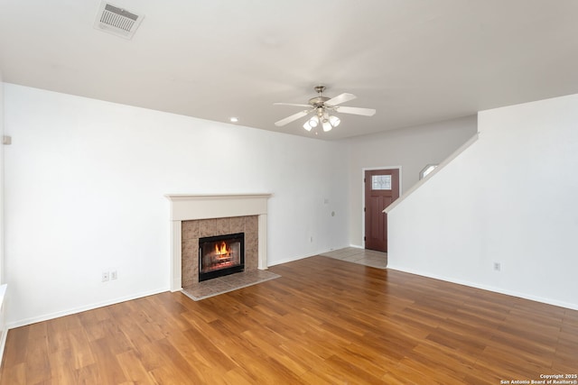 unfurnished living room featuring hardwood / wood-style floors, a tile fireplace, and ceiling fan