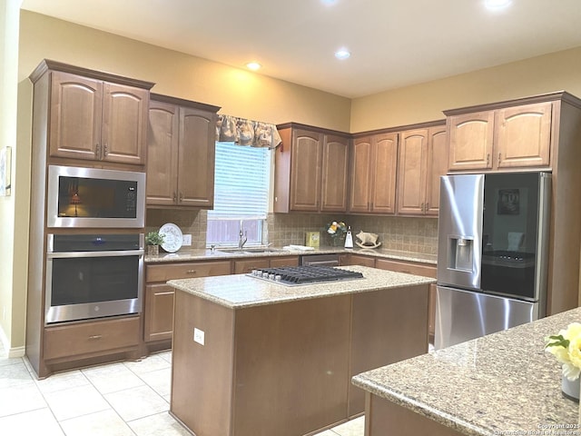 kitchen with appliances with stainless steel finishes, sink, backsplash, a center island, and light stone counters