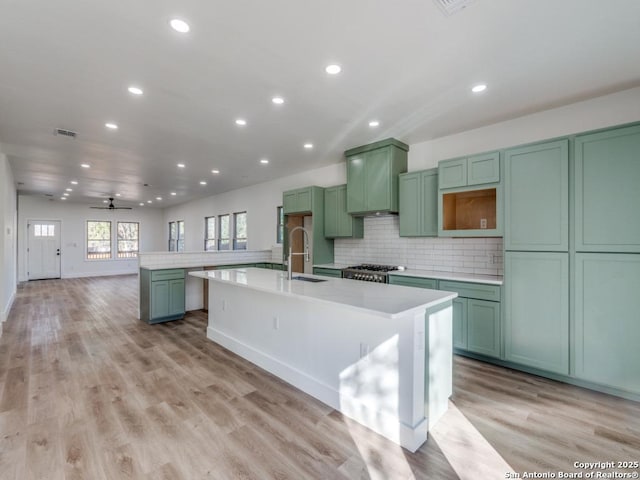 kitchen with green cabinetry, a kitchen island with sink, light hardwood / wood-style floors, and decorative backsplash