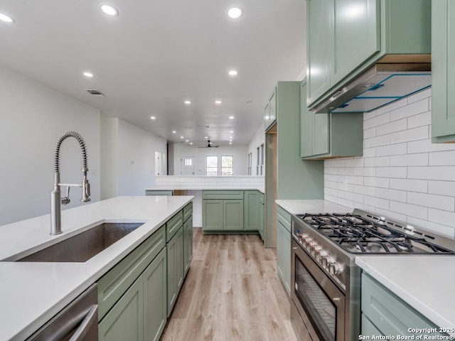 kitchen featuring sink, backsplash, green cabinets, light hardwood / wood-style floors, and stainless steel appliances