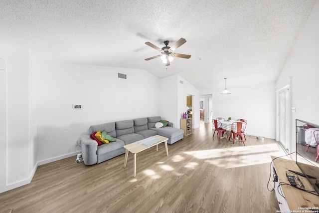 living room with lofted ceiling, hardwood / wood-style floors, a textured ceiling, and ceiling fan