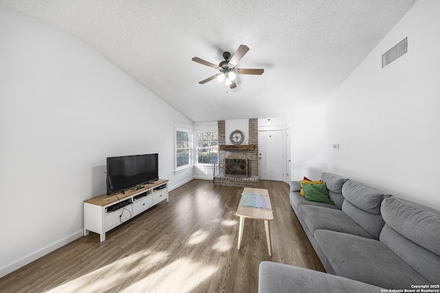 living room with dark wood-type flooring, ceiling fan, a fireplace, a textured ceiling, and vaulted ceiling