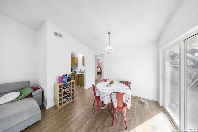 dining area with vaulted ceiling, hardwood / wood-style floors, and a textured ceiling