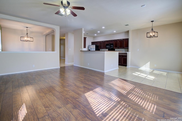 unfurnished living room featuring ceiling fan with notable chandelier and light wood-type flooring