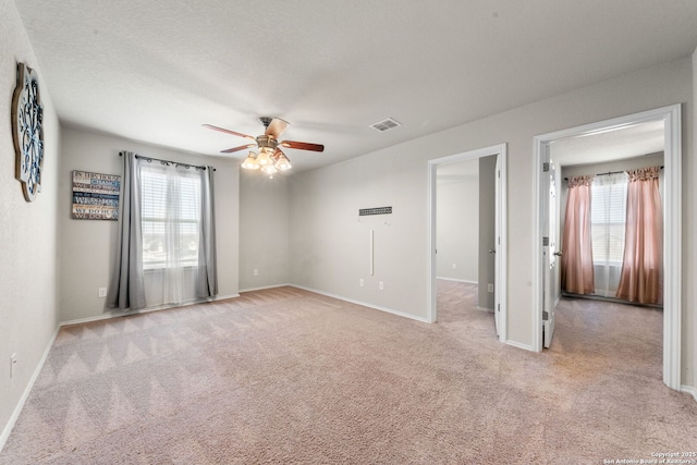 interior space with ceiling fan, light colored carpet, multiple windows, and a textured ceiling