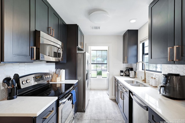 kitchen with tasteful backsplash, appliances with stainless steel finishes, sink, and light stone counters