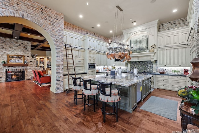 kitchen with a large island, decorative light fixtures, beamed ceiling, a fireplace, and light stone countertops