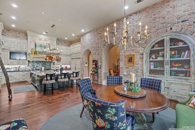 dining space with a high ceiling, brick wall, dark wood-type flooring, and a notable chandelier