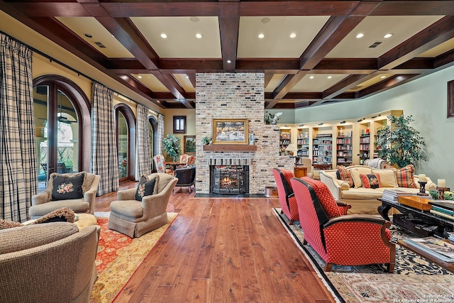 living room featuring coffered ceiling, a brick fireplace, wood-type flooring, and beamed ceiling