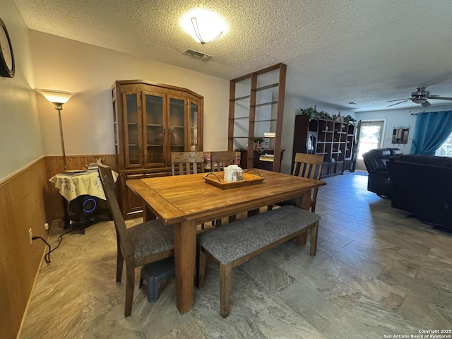 dining room with ceiling fan, wooden walls, and a textured ceiling