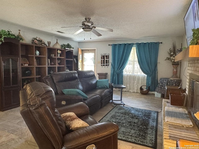 living room featuring ceiling fan, a brick fireplace, and a textured ceiling