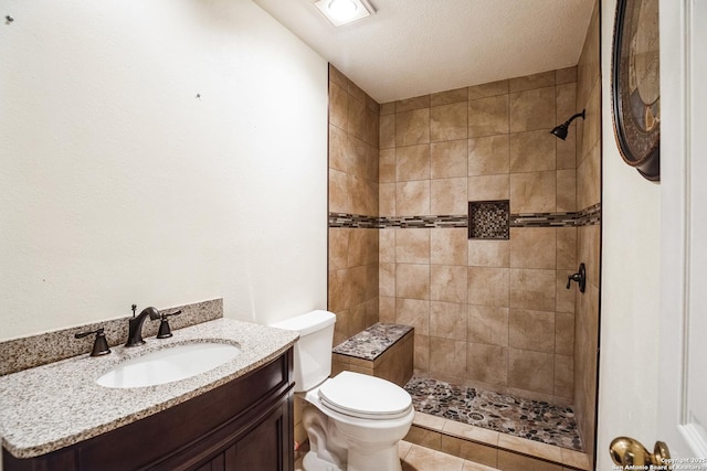 bathroom featuring vanity, a tile shower, a textured ceiling, tile patterned floors, and toilet