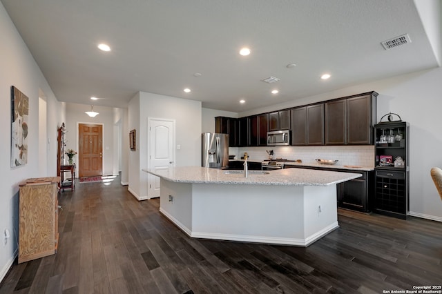 kitchen featuring a kitchen island with sink, light stone counters, tasteful backsplash, and appliances with stainless steel finishes