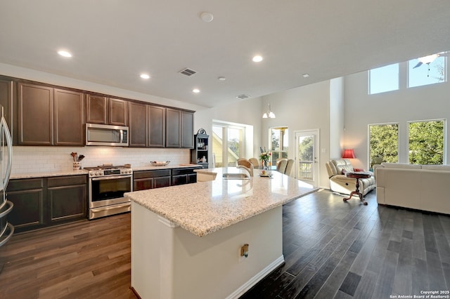 kitchen with sink, stainless steel appliances, dark brown cabinetry, a center island with sink, and decorative backsplash