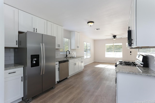 kitchen featuring appliances with stainless steel finishes, light stone counters, white cabinets, decorative backsplash, and light wood-type flooring