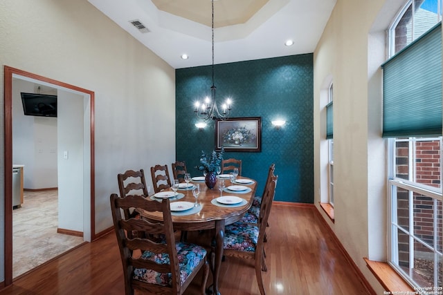 dining space with an inviting chandelier, a healthy amount of sunlight, a tray ceiling, and hardwood / wood-style floors