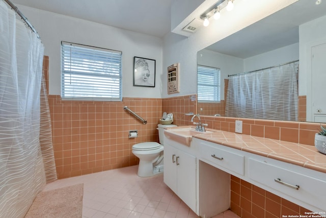 bathroom with a wainscoted wall, tile walls, toilet, vanity, and tile patterned floors