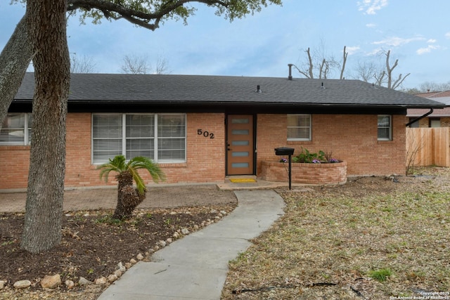 view of front of house with a shingled roof, brick siding, and fence